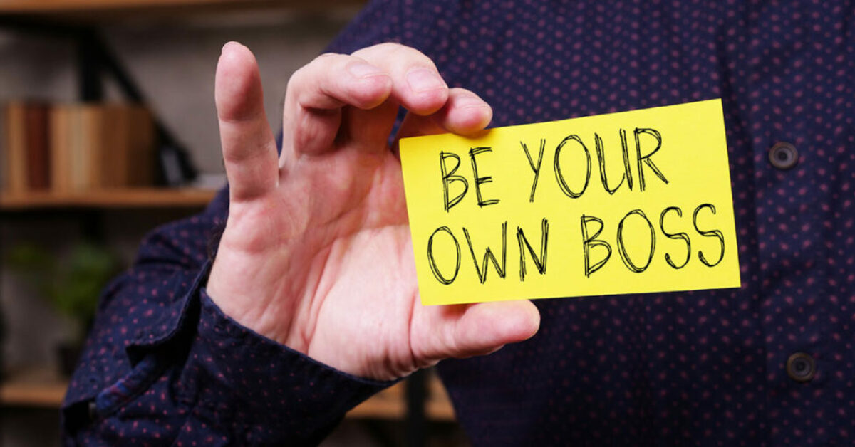 A person holding a piece of paper with the words "Be your own boss"