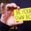 A person holding a piece of paper with the words "Be your own boss"