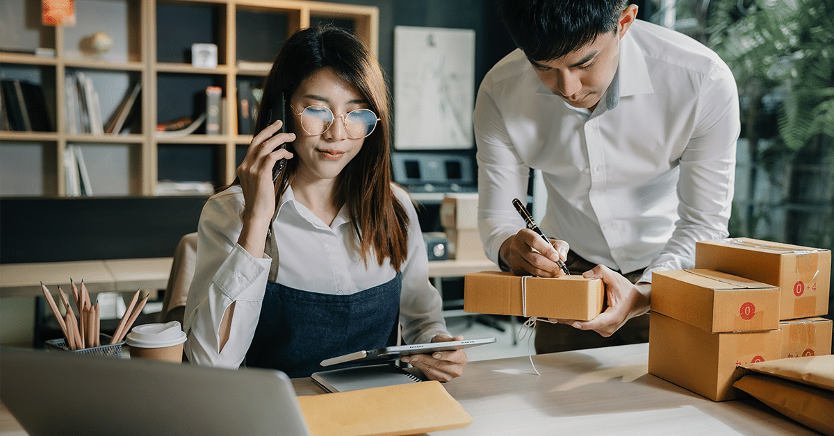 Two persons working in a small business packing parcels showing how to buy and own small business.